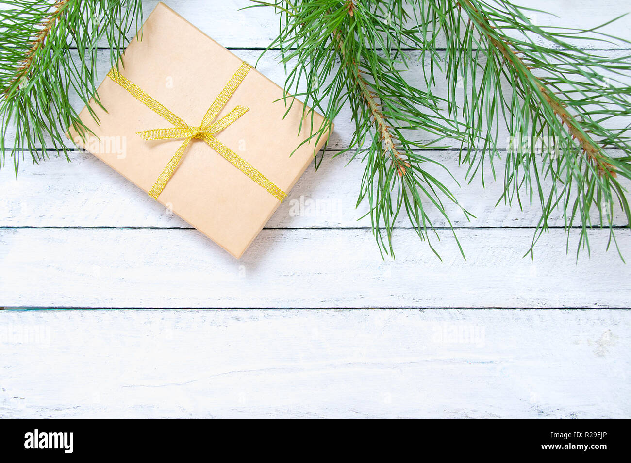 A Christmas gift in a kraft box and a spruce branch. On a white wooden background. Stock Photo