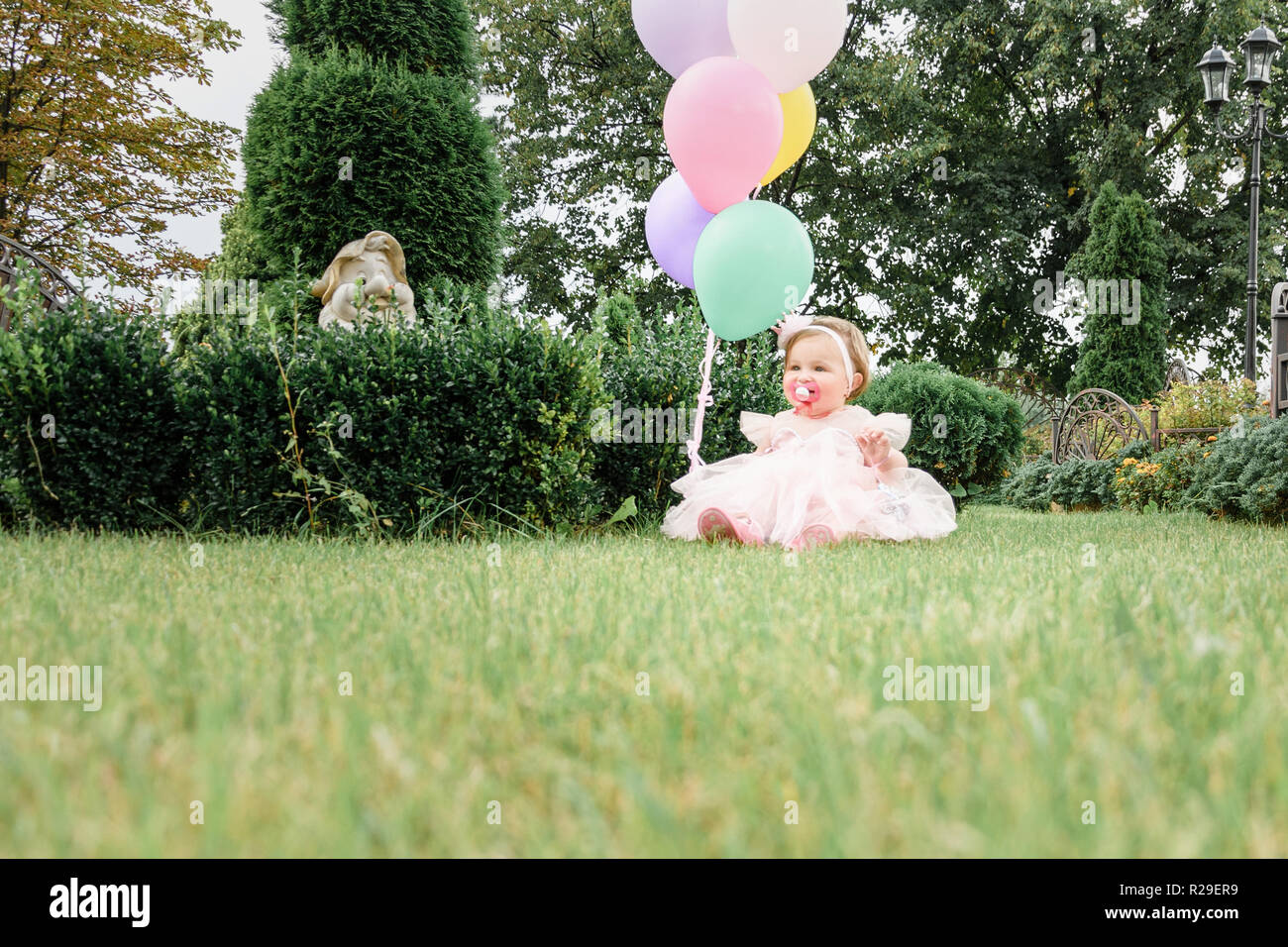 baby birthday girl holding balloons in the yard 18 Stock Photo