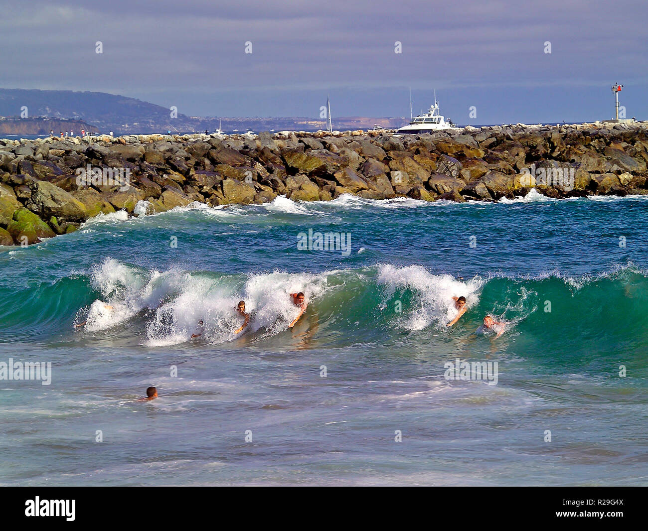 Bodysurfers ride Pacific Ocean surf at The Wedge on the Balboa Peninsula, where extreme waves form next to the rock jetty that protects the boat channel entrance to Newport Harbor at Newport Beach in Orange County, Southern California, USA. Stock Photo