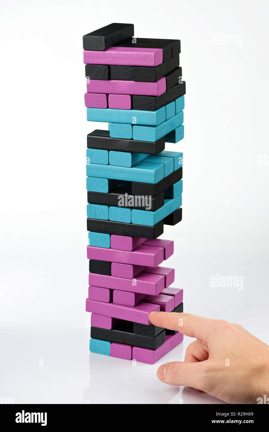 Playing wooden tower game on white background. Hand take one brick from balancing tower Stock Photo