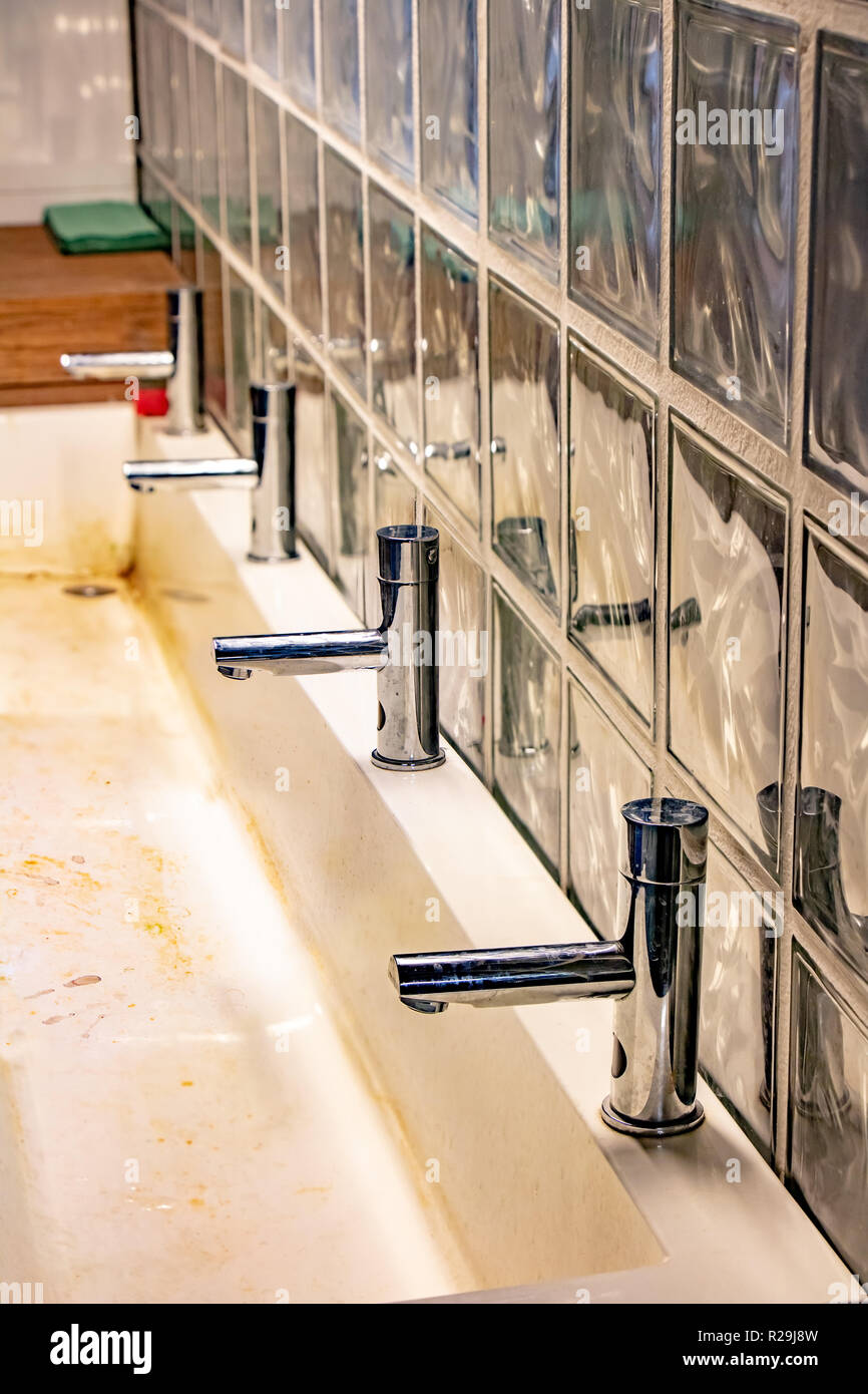 A dirty basin in public bathroom. Long washbasin with a row of water taps. Stock Photo