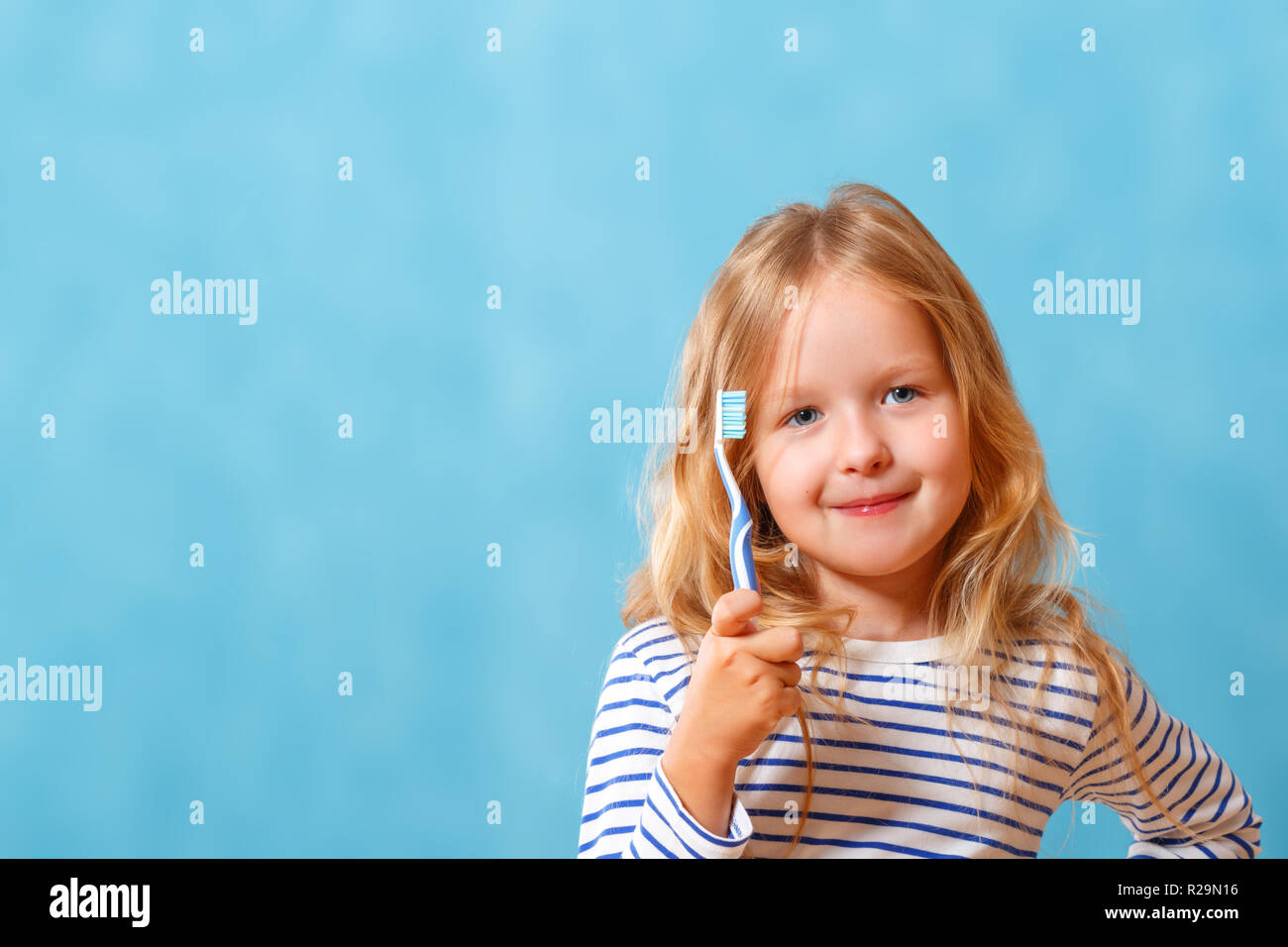 A little girl in striped pajamas is brushing her teeth with a