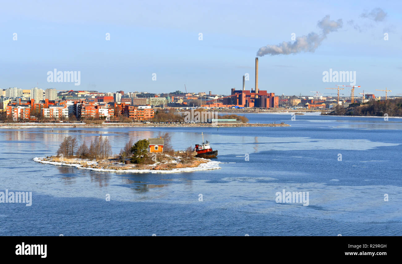 Small rocky island of Helsinki archipelago against  backdrop of industrial area of city. Finland Stock Photo