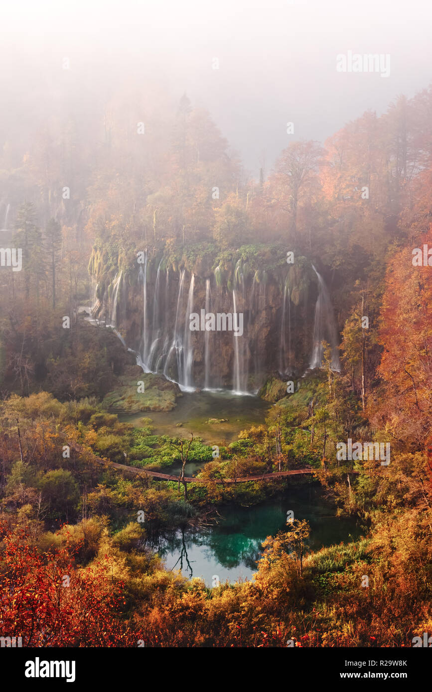 Aerial view on amazing foggy waterfall in Plitvice lakes. Orange autumn forest on background. Plitvice National Park, Croatia. Landscape photography Stock Photo