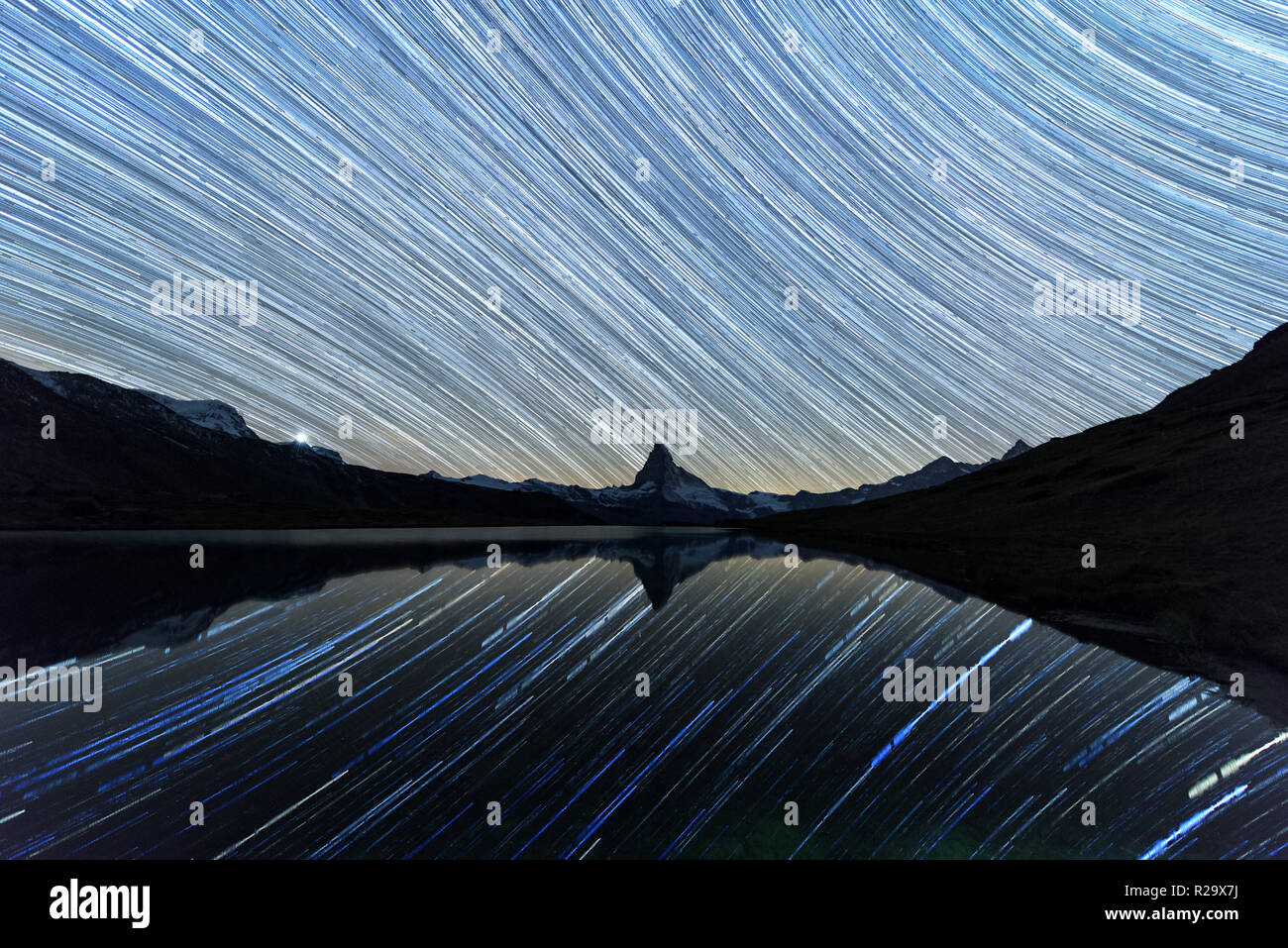 Incredible night view of Stellisee lake with Matterhorn Cervino peak in Swiss Alps. Stars trails moving in blue sky. Zermatt resort location, Switzerl Stock Photo