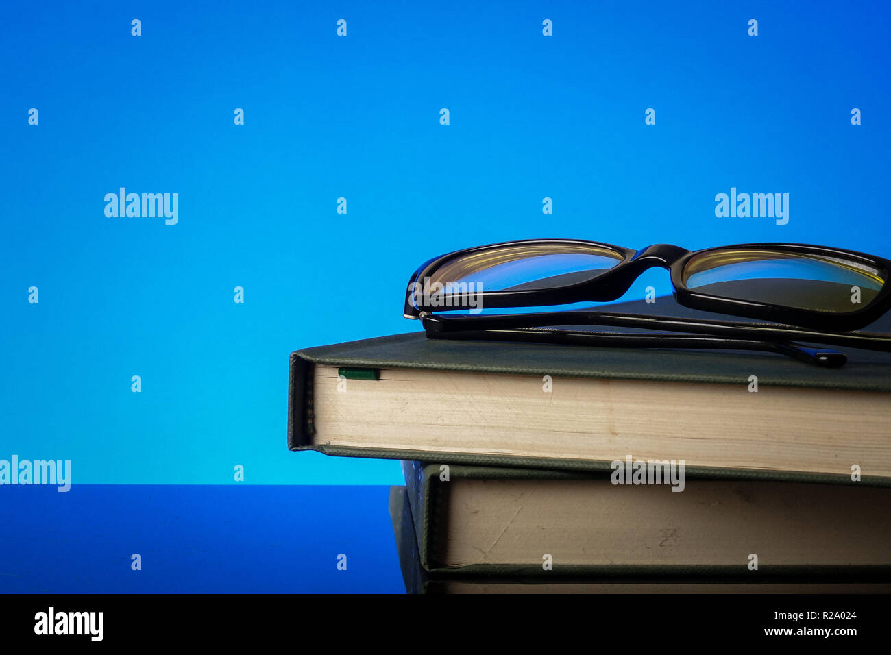 EDUCATION CONCEPT with stack of old book and reading glasses on a blue background. Stock Photo