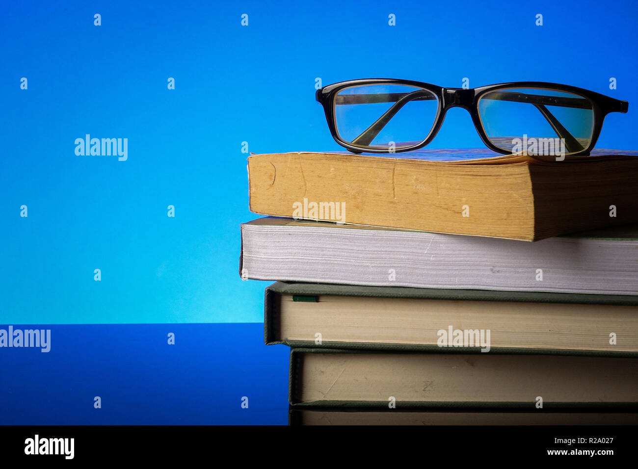 EDUCATION CONCEPT with stack of old book and reading glasses on a blue background. Stock Photo
