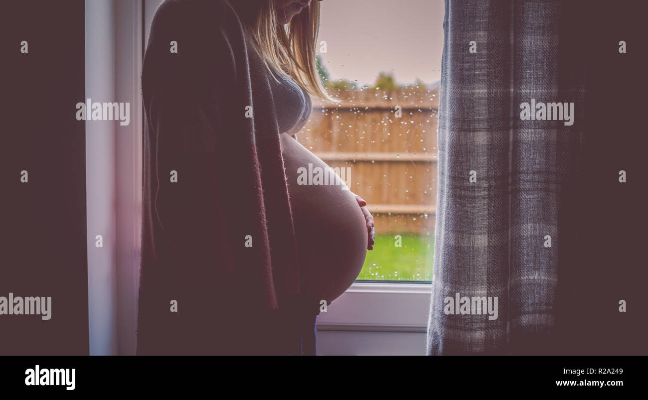 Side view of pregnant woman stood in front of window Stock Photo