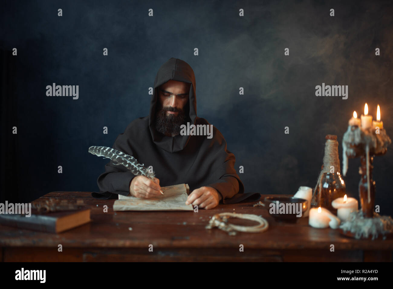 Medieval monk in robe and hood writes with a goose feather, black ...