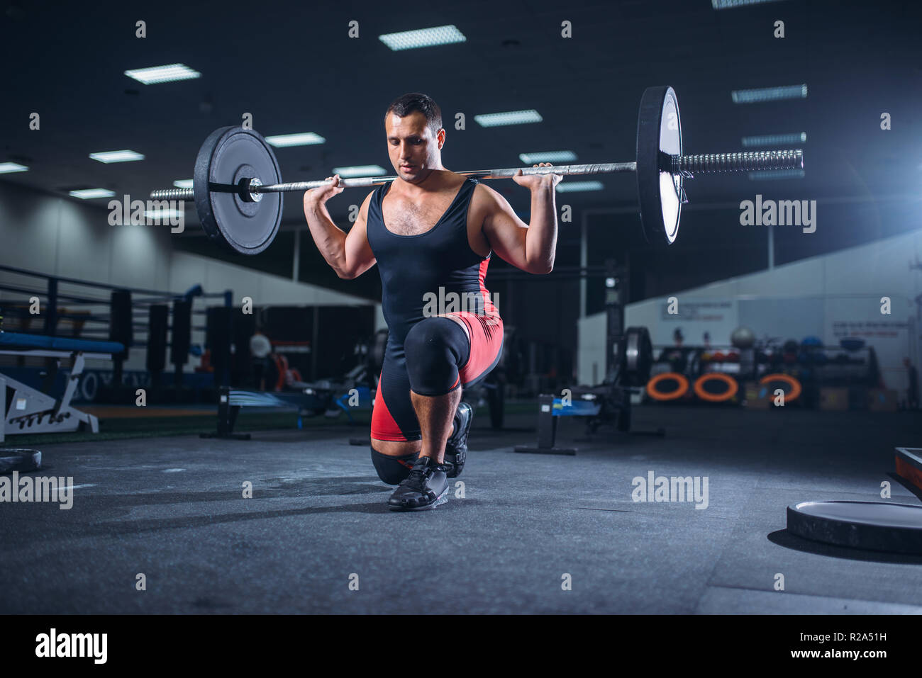 Strong weight lifter doing squats with a barbell in gym, deadlift