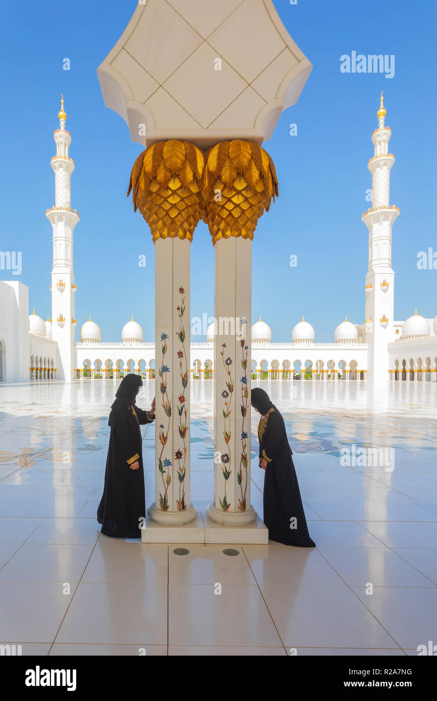 2 Arab women wearing traditional black abaya while praying in Sheikh Zayed Mosque in Abu Dhabi, United Arab Emirates with minarets in background Stock Photo