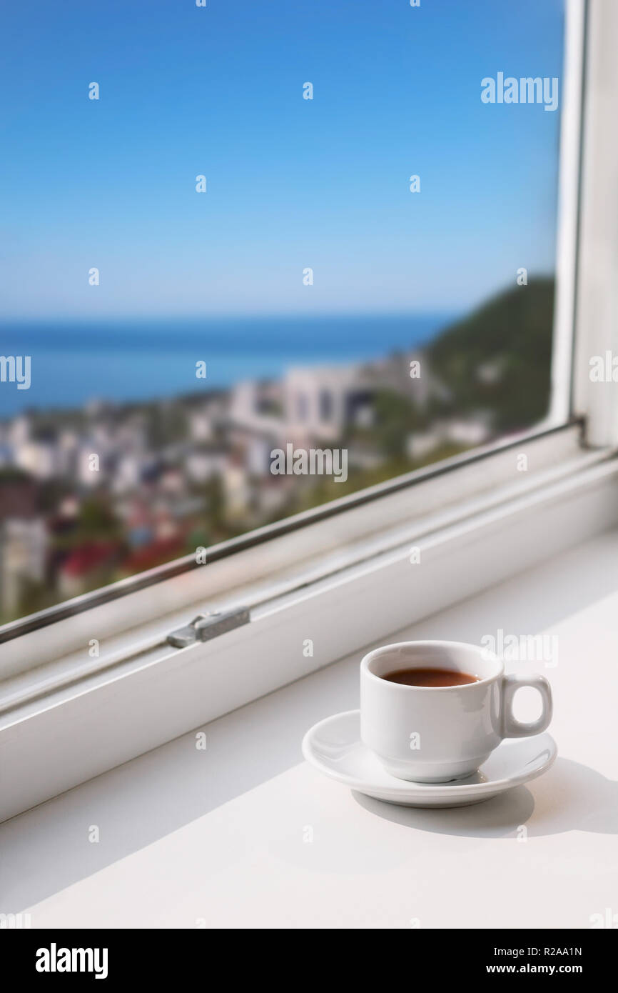 white cup with drink on a window sill with blurred city view with  blue sky and sea copy space Stock Photo