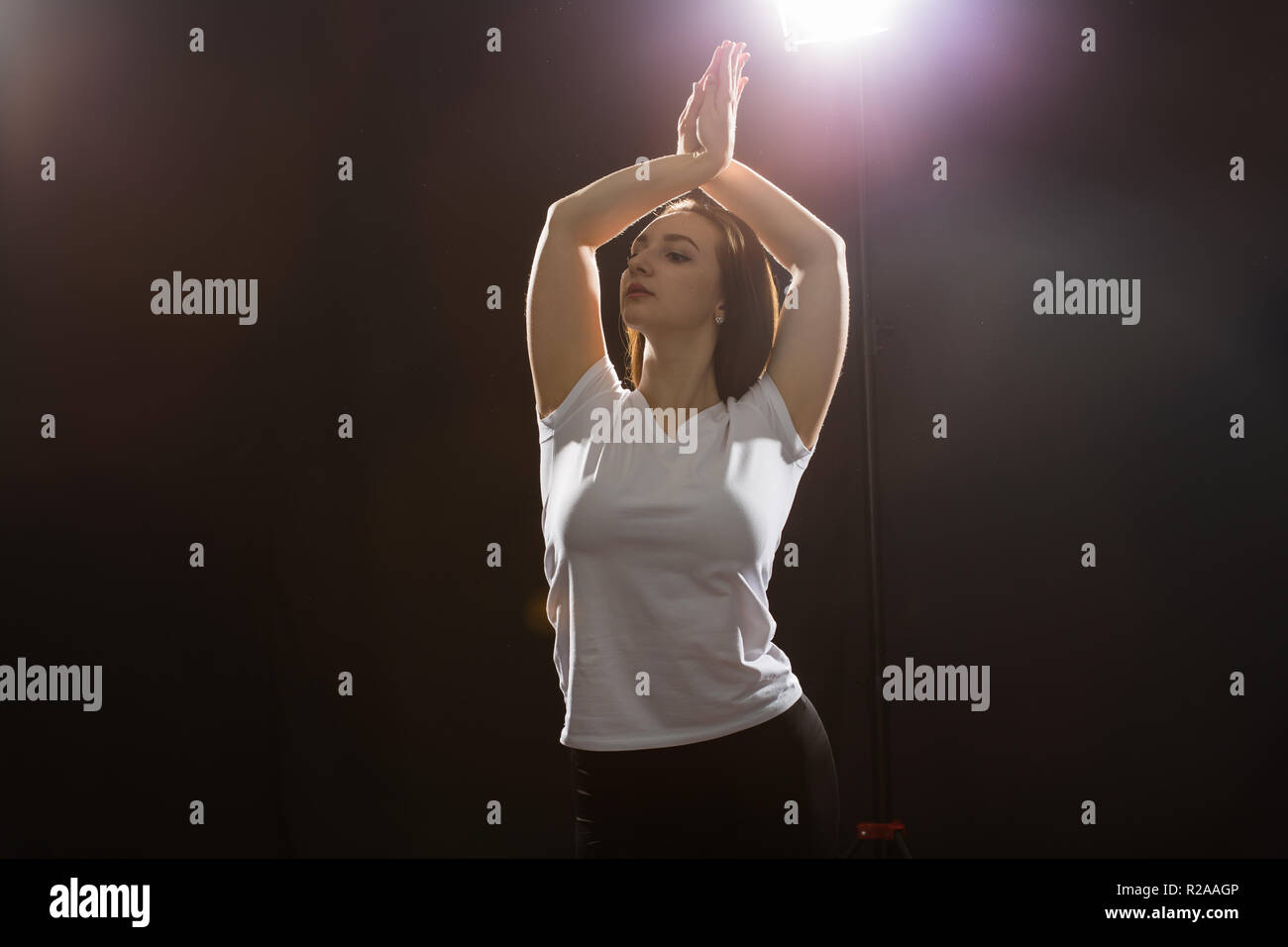 Dancing, jazz-funk and hip-hop concept - young woman dancing in darkness and folded her arms over her head Stock Photo