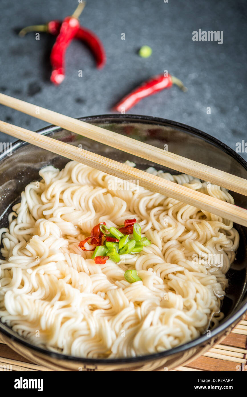 Black bowl of asian instant noodles with hot water and red chili peppers and green onion and chopsticks Stock Photo