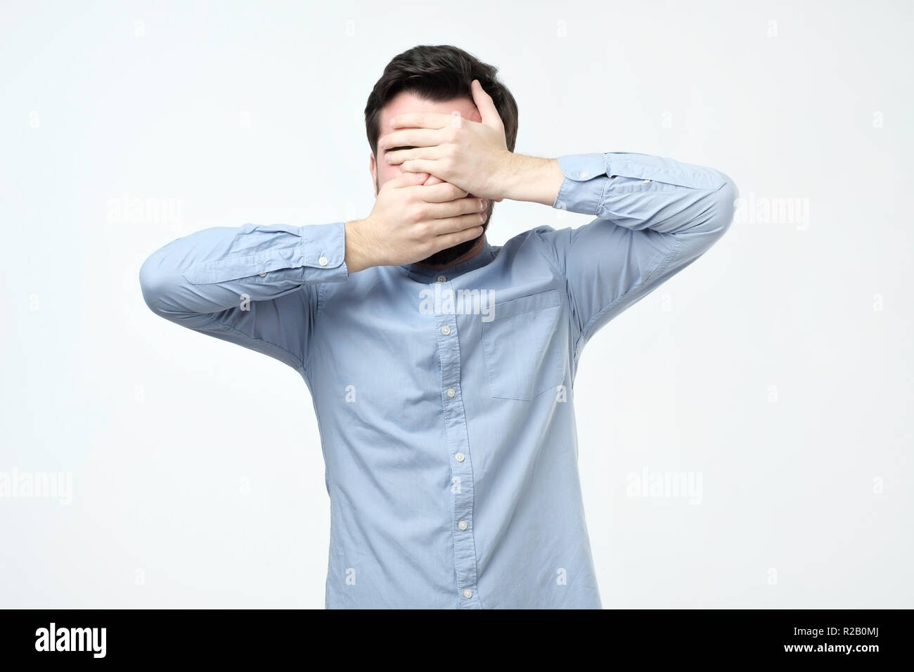 Man in blue shirt covered his face with his hands Stock Photo - Alamy