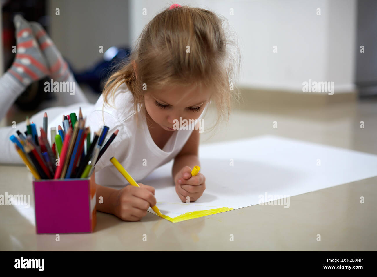 Adorable little girl lying on floor and drawing on huge paper sheet with yellow marker pen Stock Photo