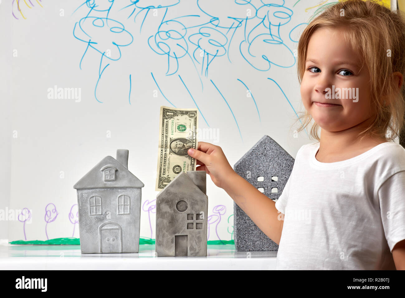 Girl with money standing near toy houses Stock Photo