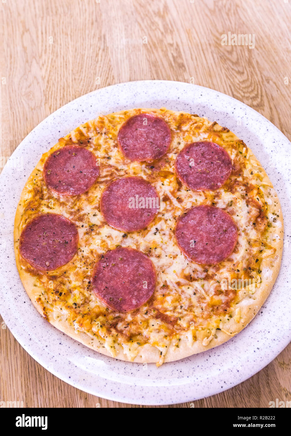 Prepared from frozen, typical salami pizza on plate on wooden background Stock Photo