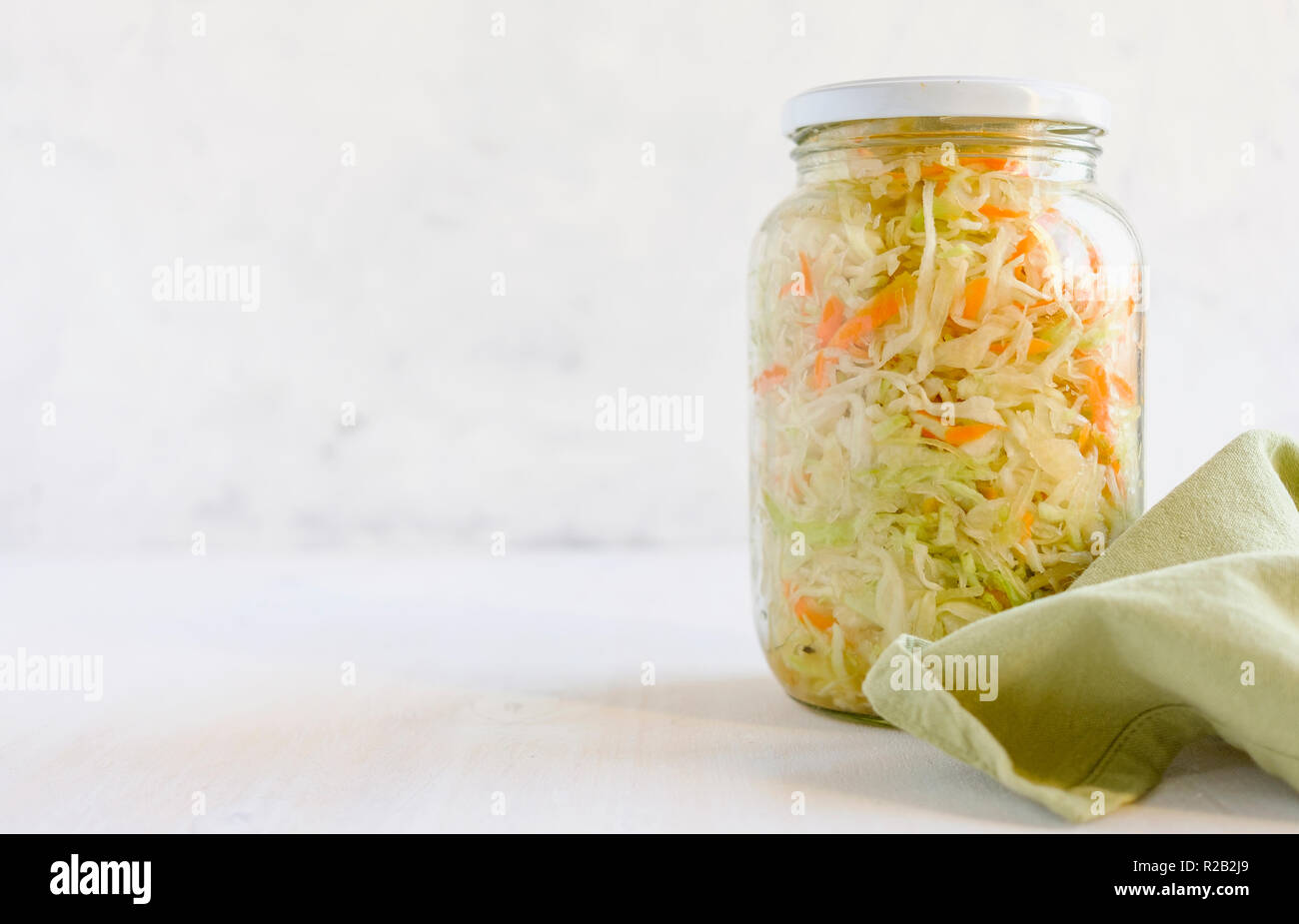Sealed glass jar with delectable fermented cabbage standing on piece of cloth on white background Stock Photo