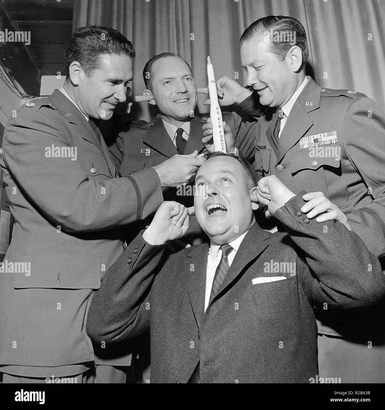 Some U.S. Air Force officers get goofy with a rocket on a man's head, ca. 1960. Stock Photo