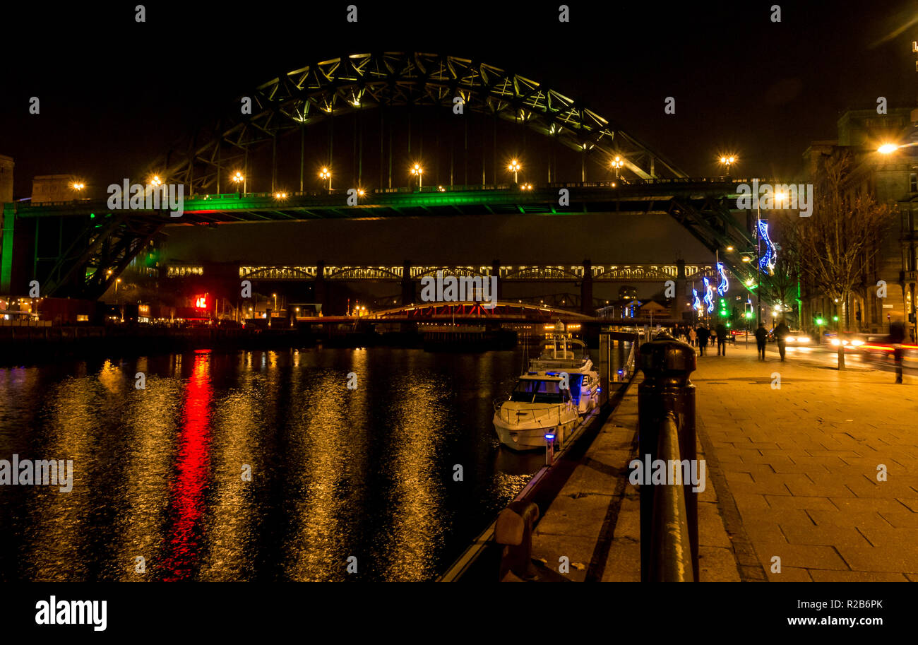 River Tyne at night with lights on swing bridge, high level bridge and Tyne Bridge and people walking on riverside, Newcastle, England, UK Stock Photo