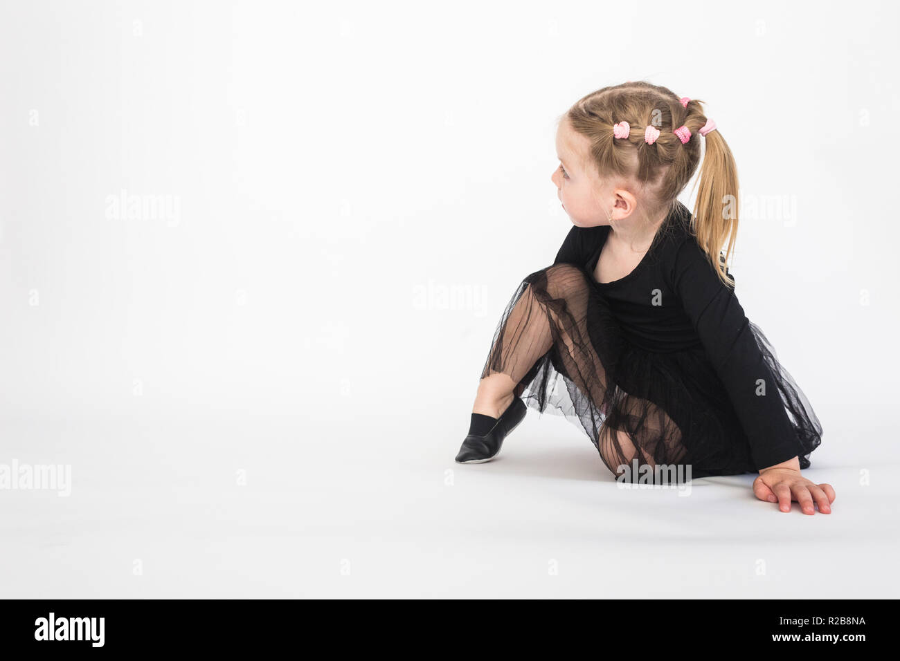 Cute little girl in beautiful black dress sitting on the floor on white ...