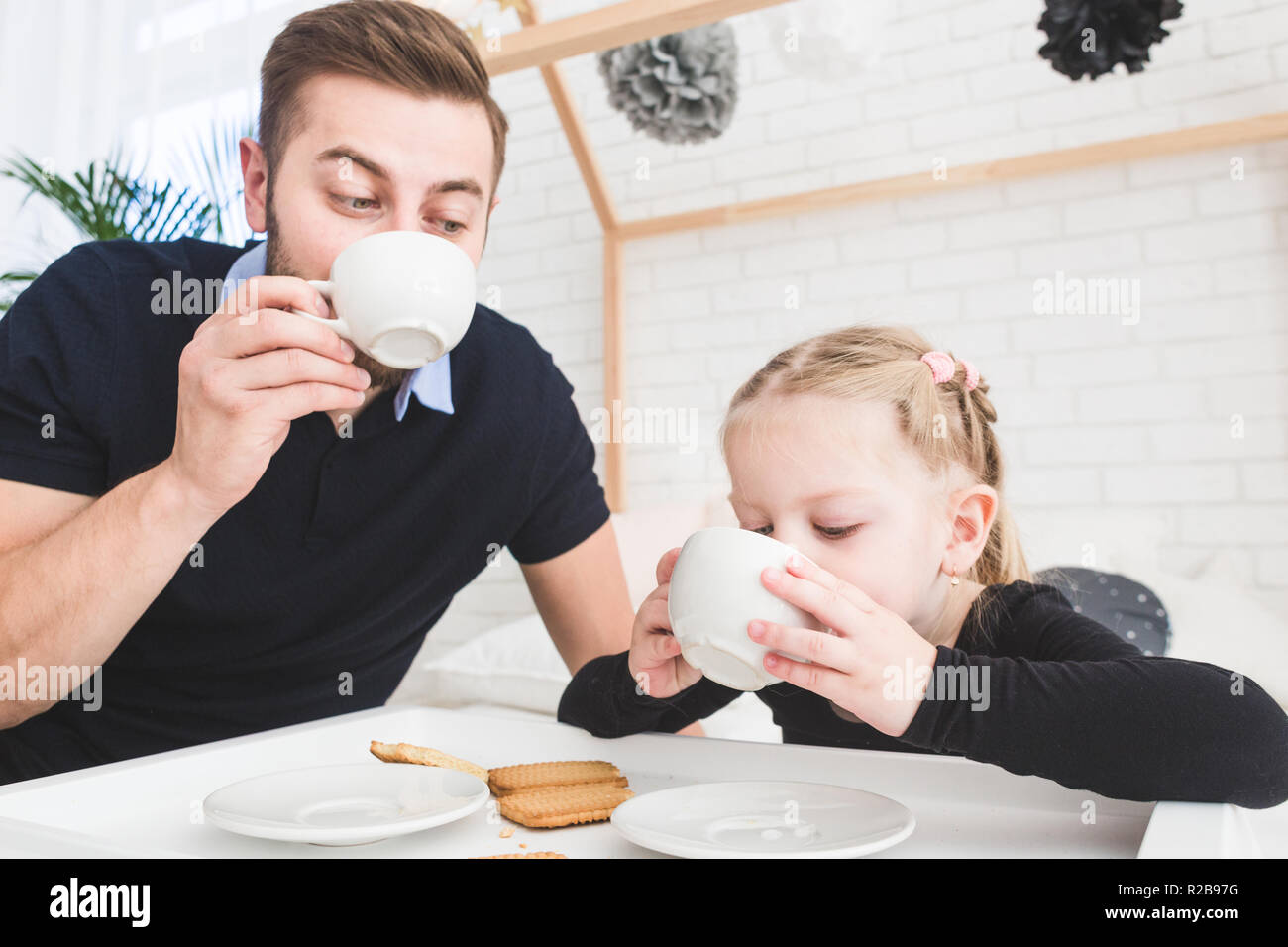 Cute little girl and her father drink tea with cookies at home. Stock Photo