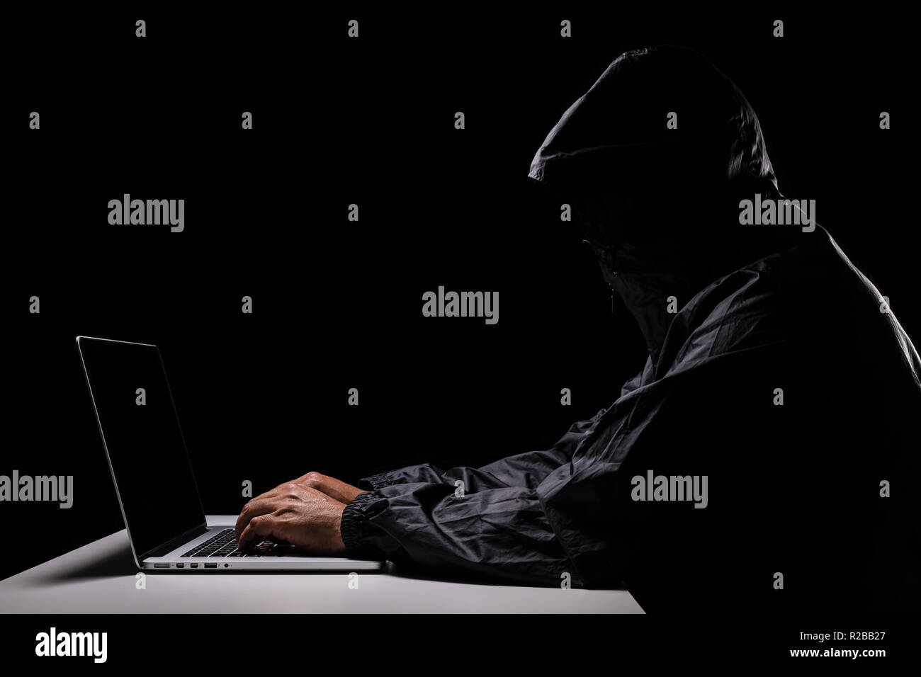 A male hacker cover his head with the hood trying to steal the data ...