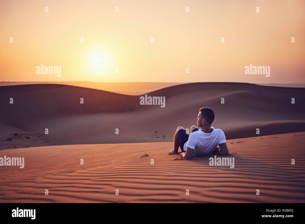 Idyllic sunrise in desert. Young man contemplation on sand dune. Wahiba Sands in Oman. Stock Photo