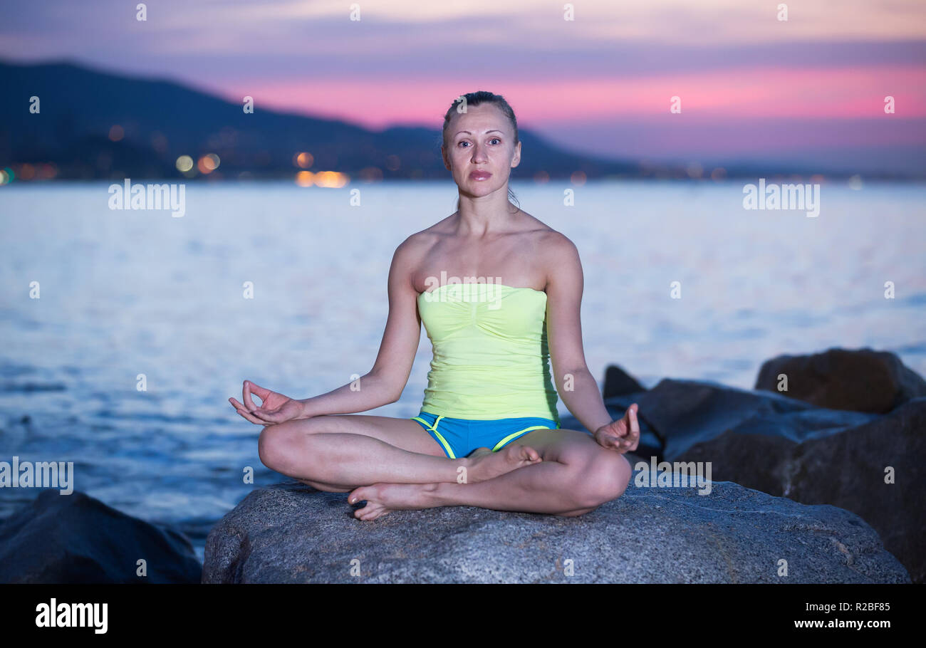 Young girl in yoga pose lotos at ocean quay Stock Photo - Alamy