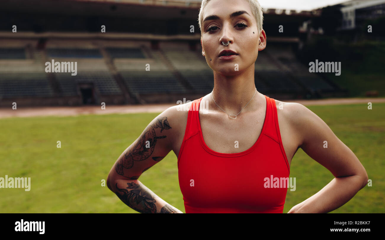 fitness woman standing inside a track and field stadium. Close up of a woman in fitness wear standing with hands on hip. Stock Photo