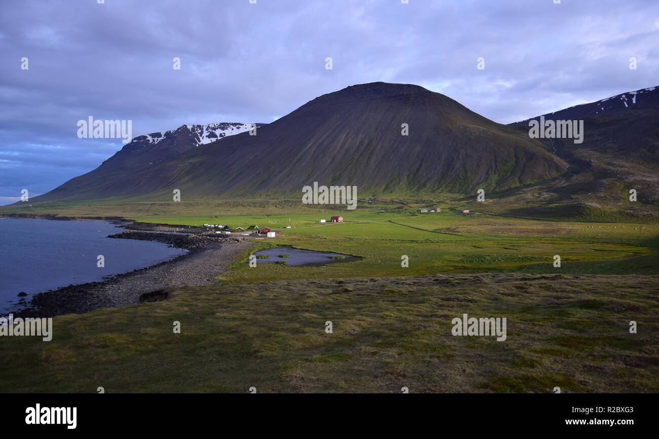 Icelandic landscape with the campsite at the hot pot Grettislaug on peninsula Skagi.A few buildings and in the background a mountain in the evening su Stock Photo