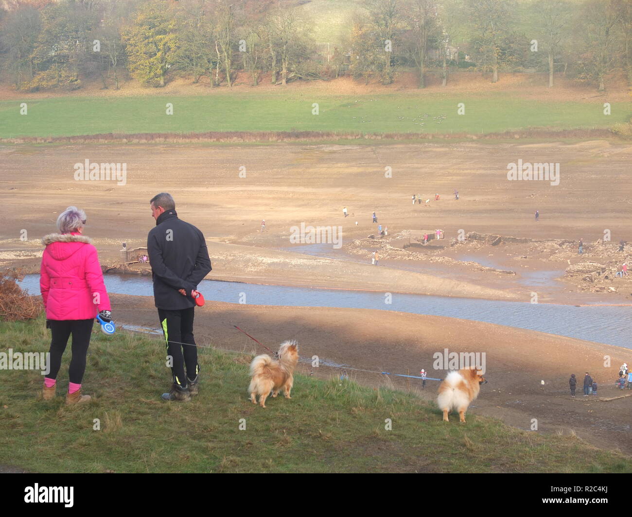 Dog walkers inspect the water levels in Ladybower Reservoir which have dropped low enough to reveal the remains of the abandoned Derwent village Stock Photo