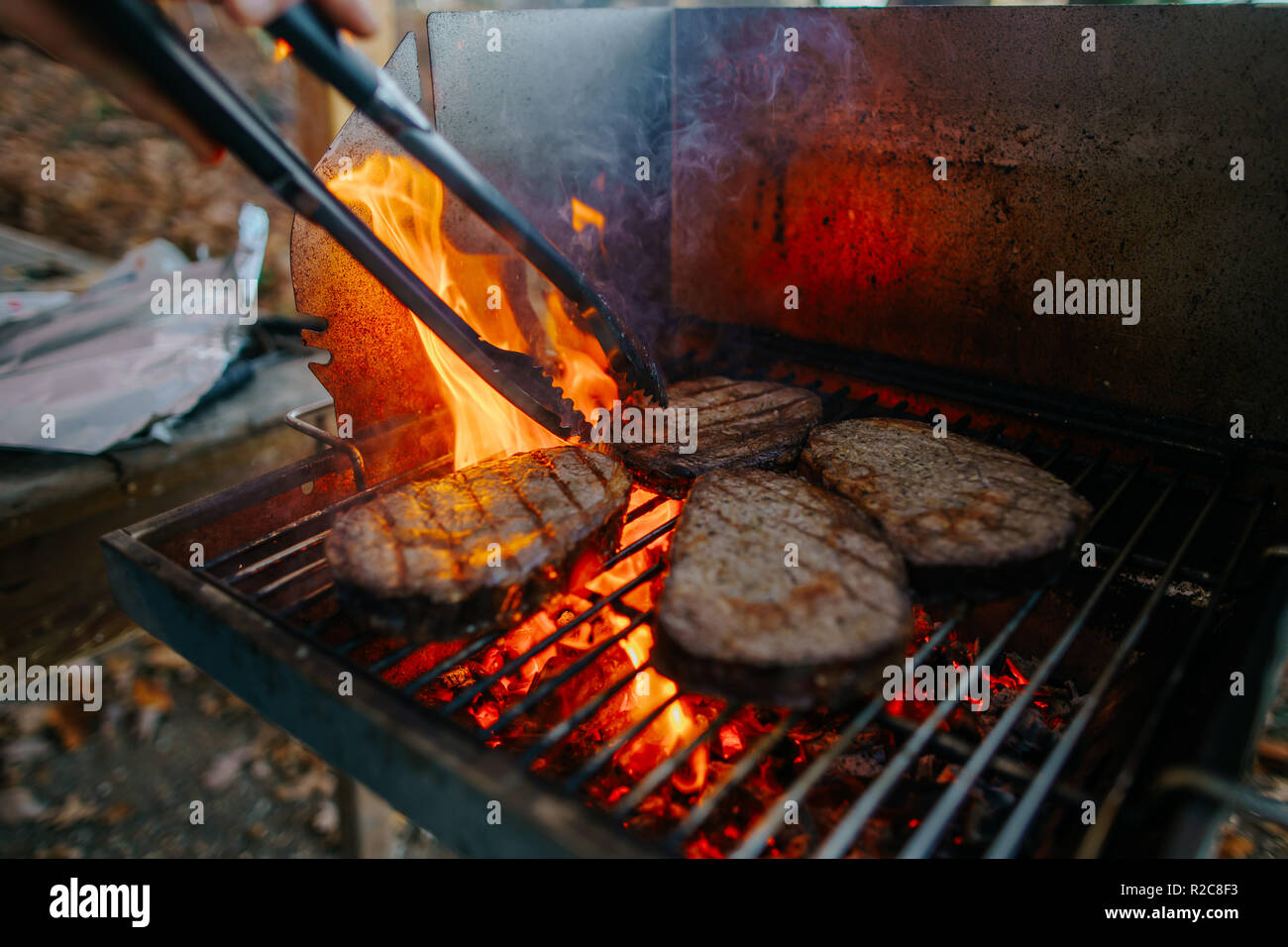 four welldone ribeyesteaks with high flames and barbecue tong on the