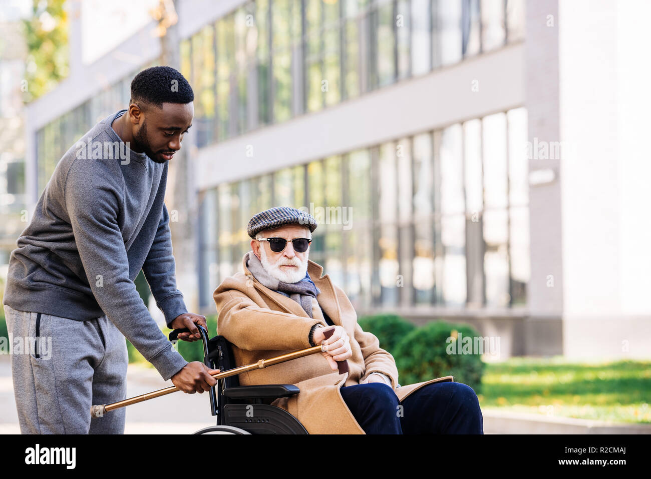 african american man giving walking stick to senior disabled man in