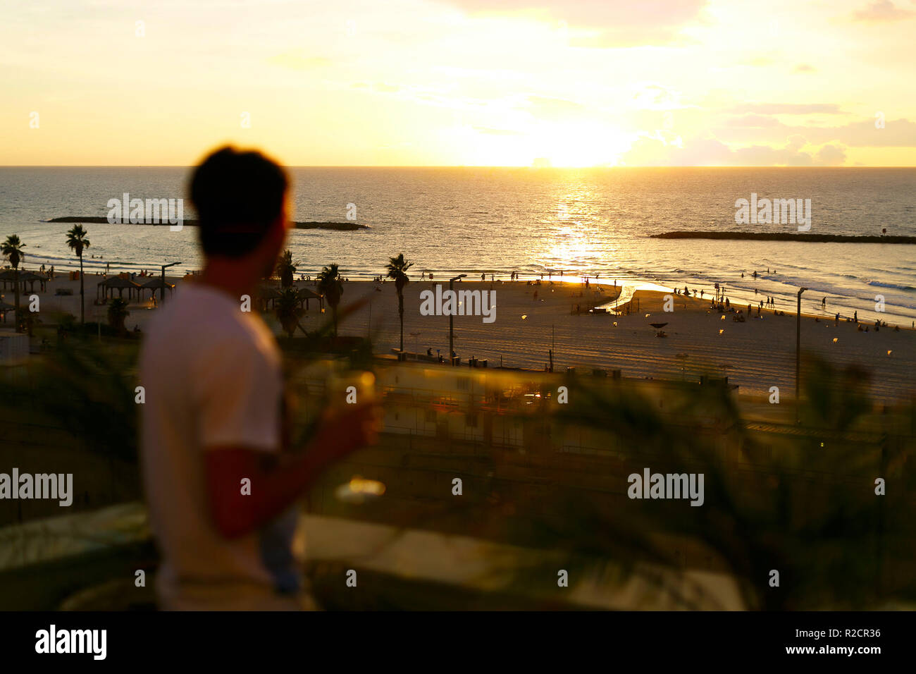 beautiful sunset on the beach. A young man is out of focus looking towards the sea, the silhouette of the sun. Bright colors and unique cloud formations. Stock Photo