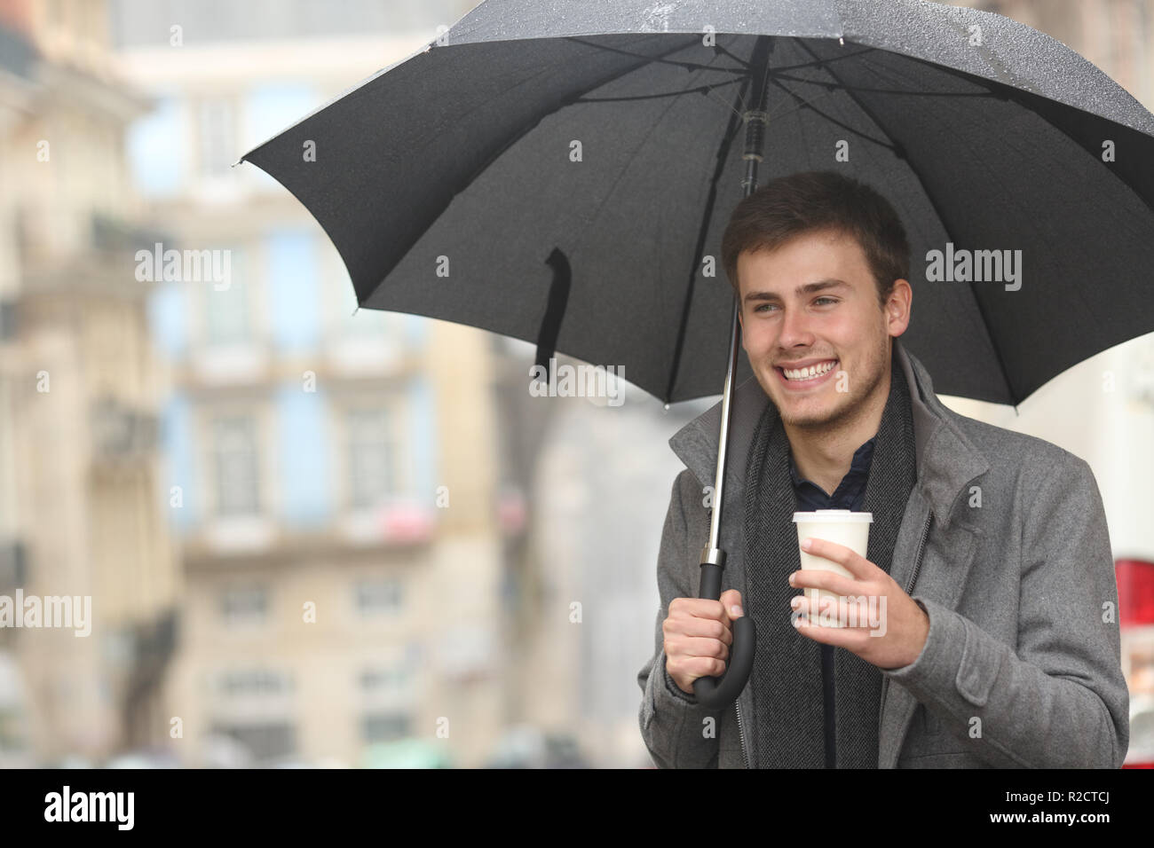 Happy man walking holding a takeaway drink in winter under the rain in the street Stock Photo