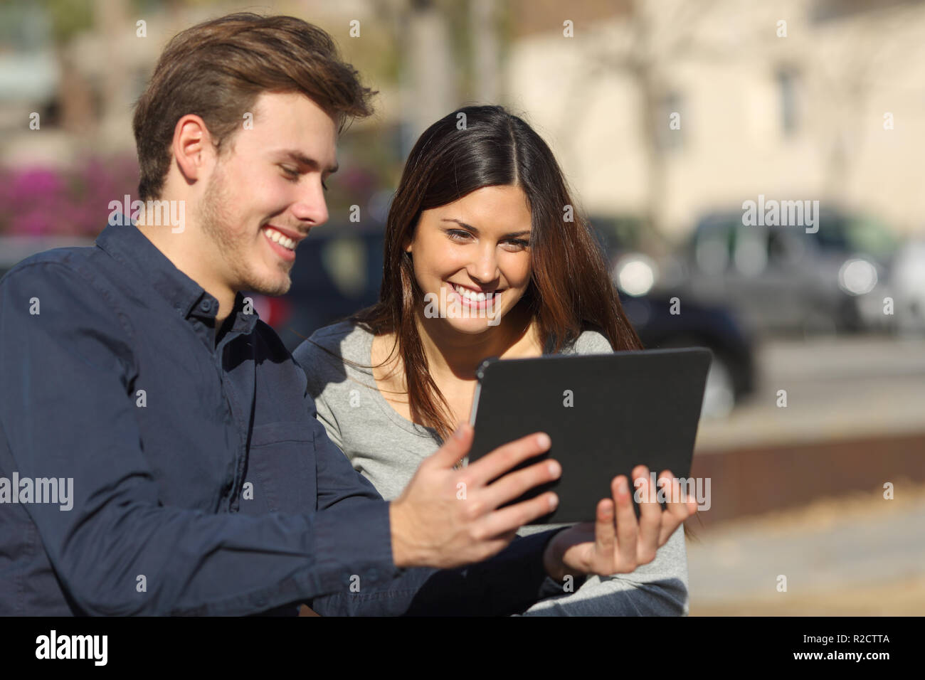 Happy couple watching media content in a tablet sitting outdoors in a park Stock Photo