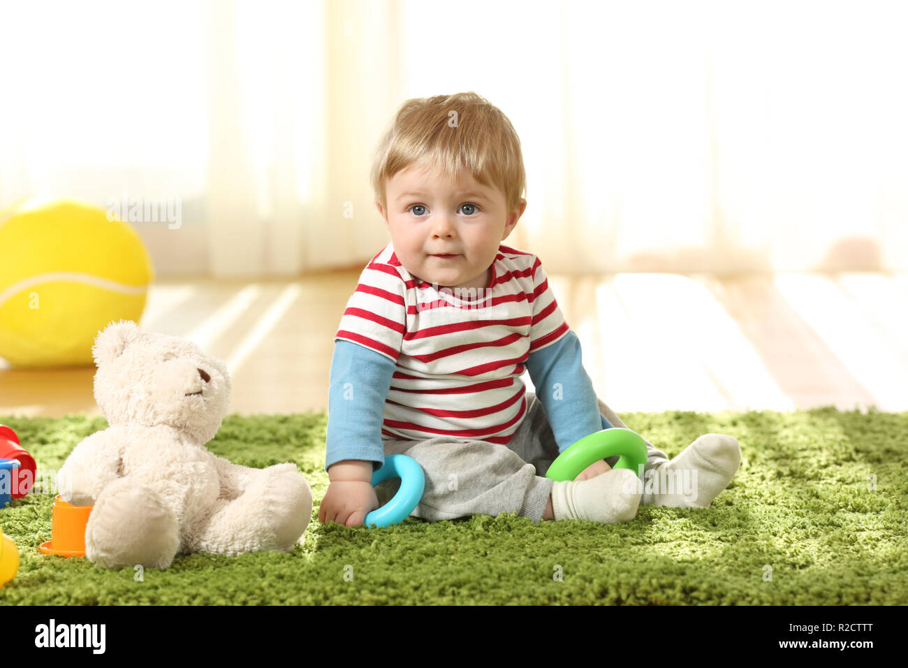 Full body portrait of a single kid sitting on a carpet on the floor with toys at home Stock Photo