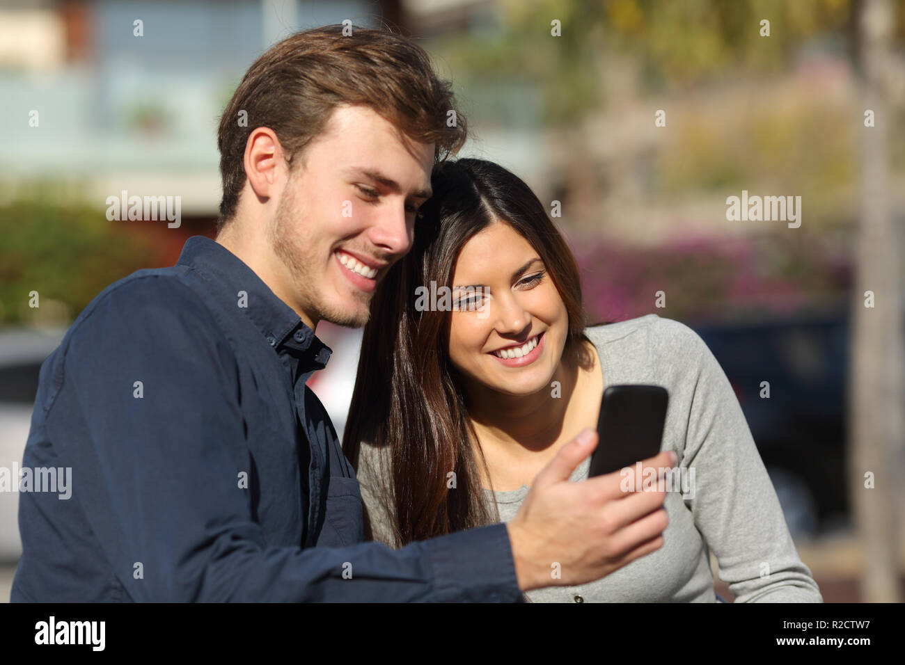 Happy couple consulting smart phone content sitting on a bench in a park Stock Photo