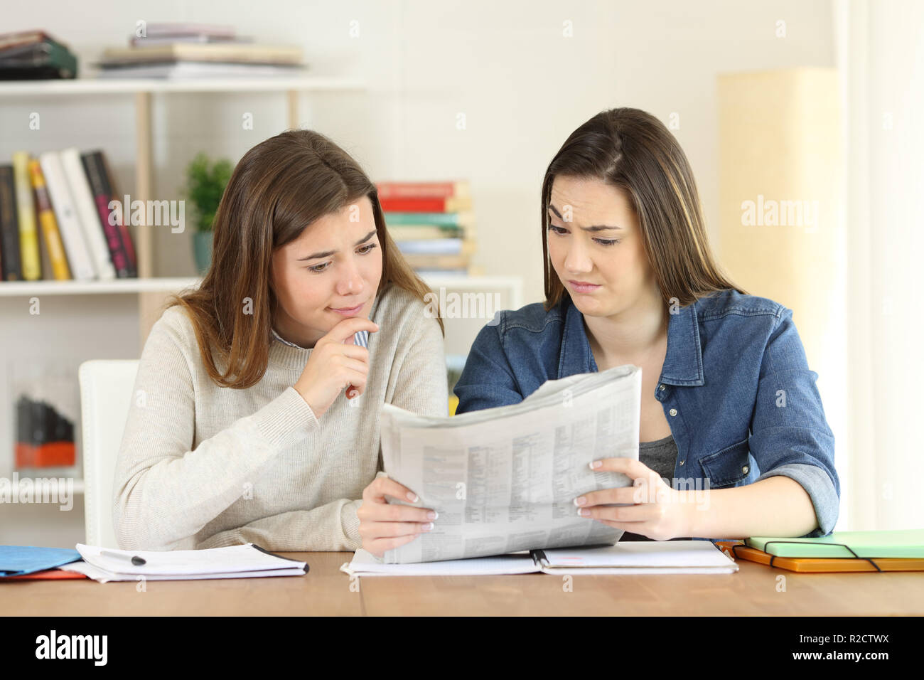 Front view portrait of two students finding suspicious news in a newspaper at home Stock Photo