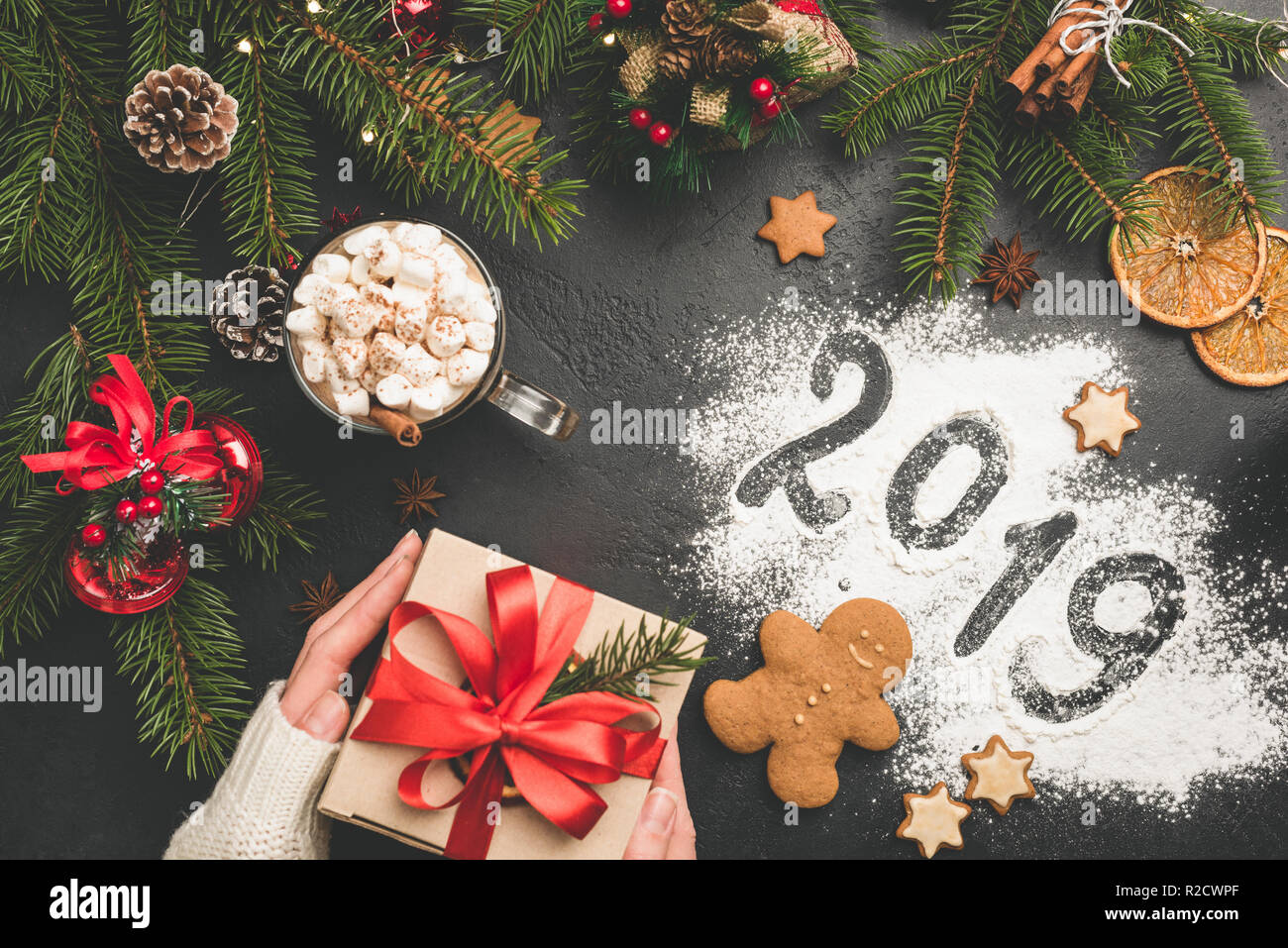 2019 Christmas or New Year background with gift box, fir tree, hot chocolate. 2019 written on flour on black concrete background. Festive Winter Holid Stock Photo