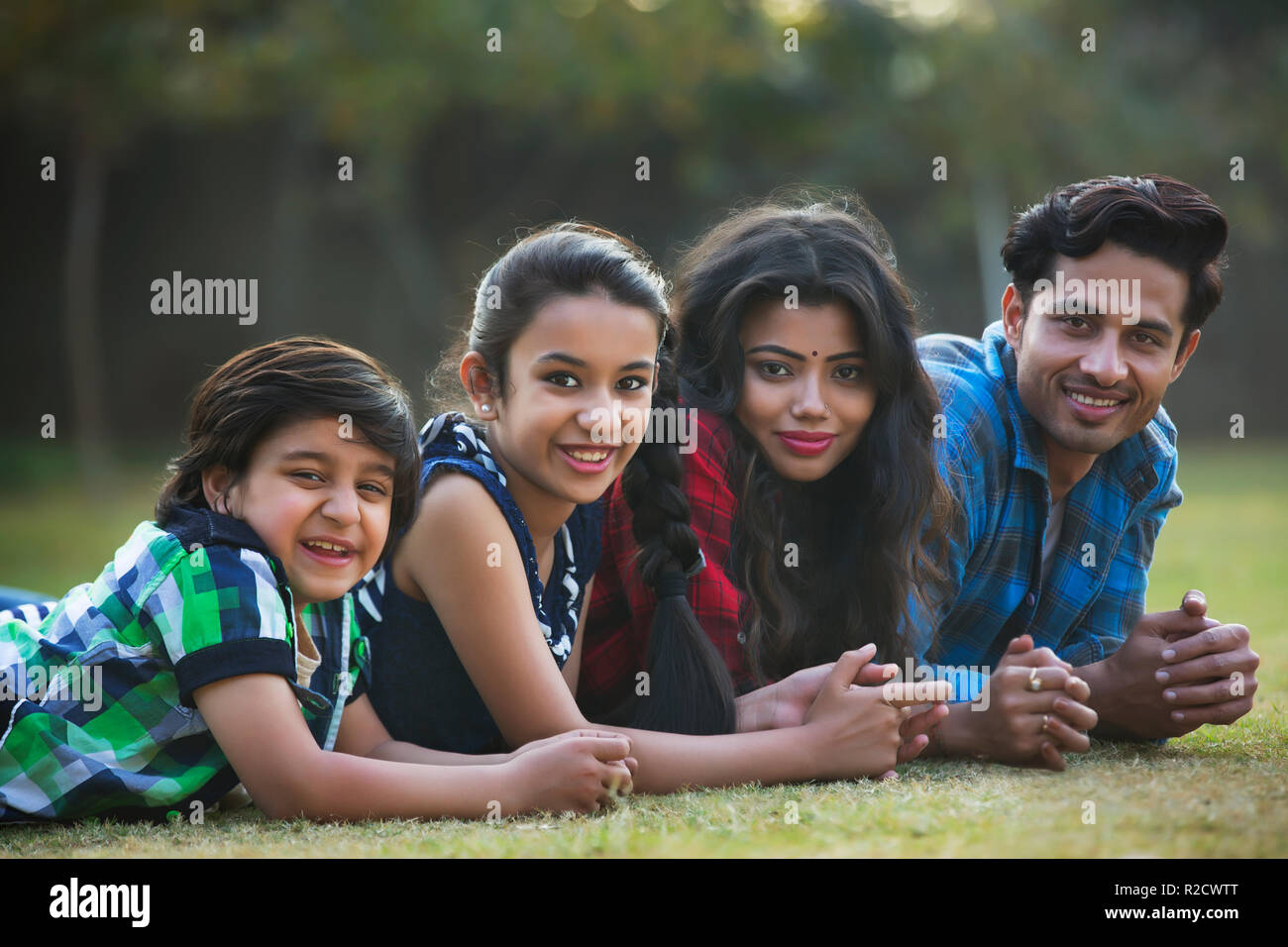 Happy family of man woman and two children lying on the ground in a park looking at camera. Stock Photo