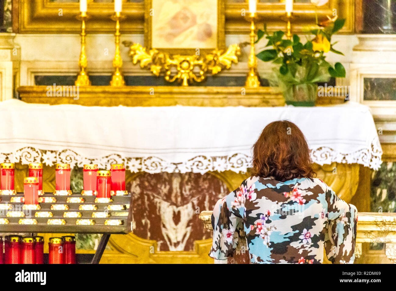 Kneeling woman praying in front of the altar of a Catholic Church Stock