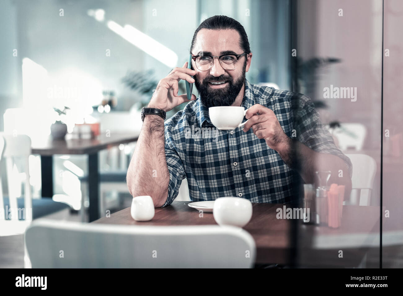 Dark-eyed man wearing squared shirt holding white cup of coffee Stock Photo