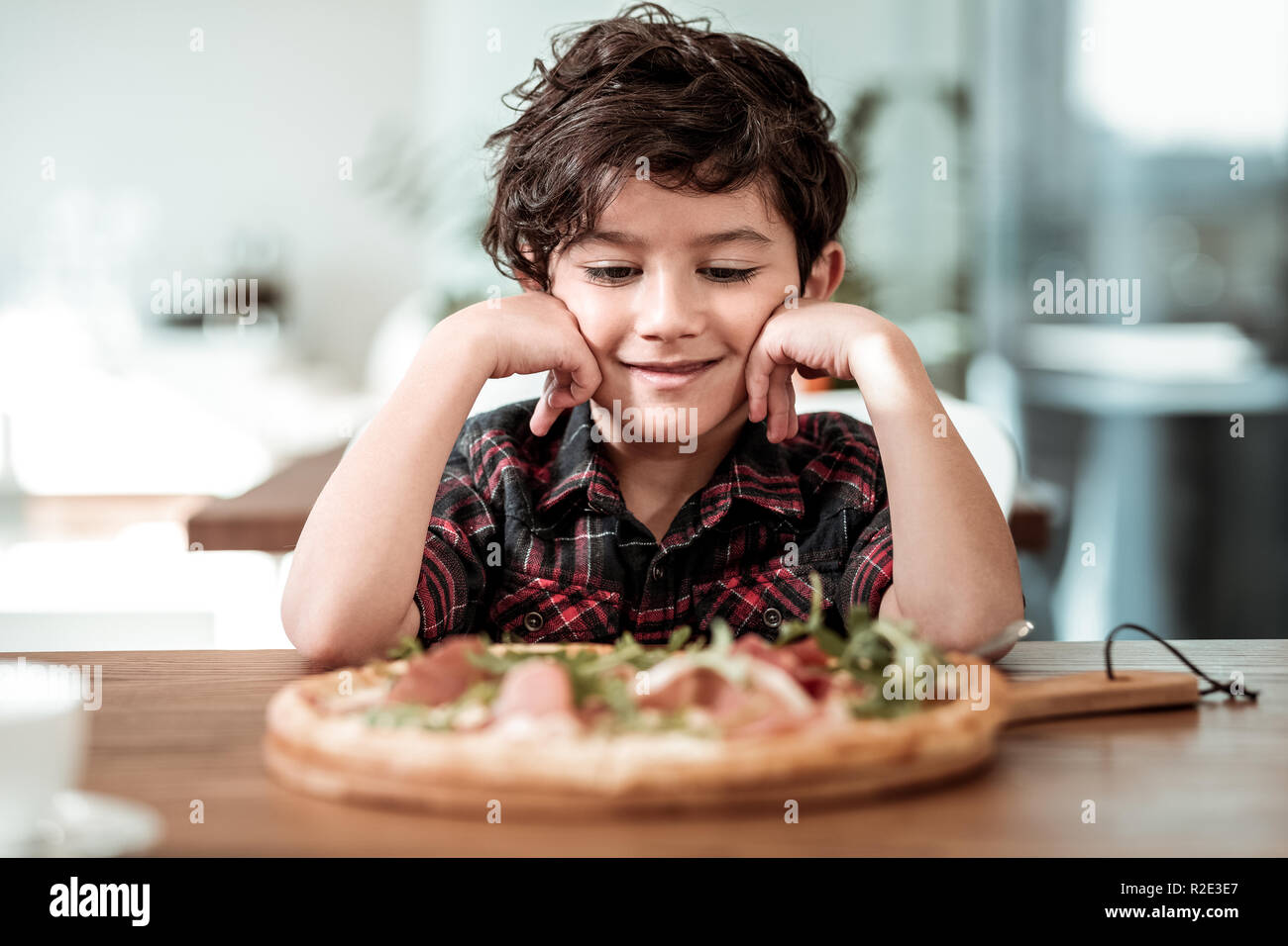 Cute preschool boy eating pizza with bacon and greenery on weekend