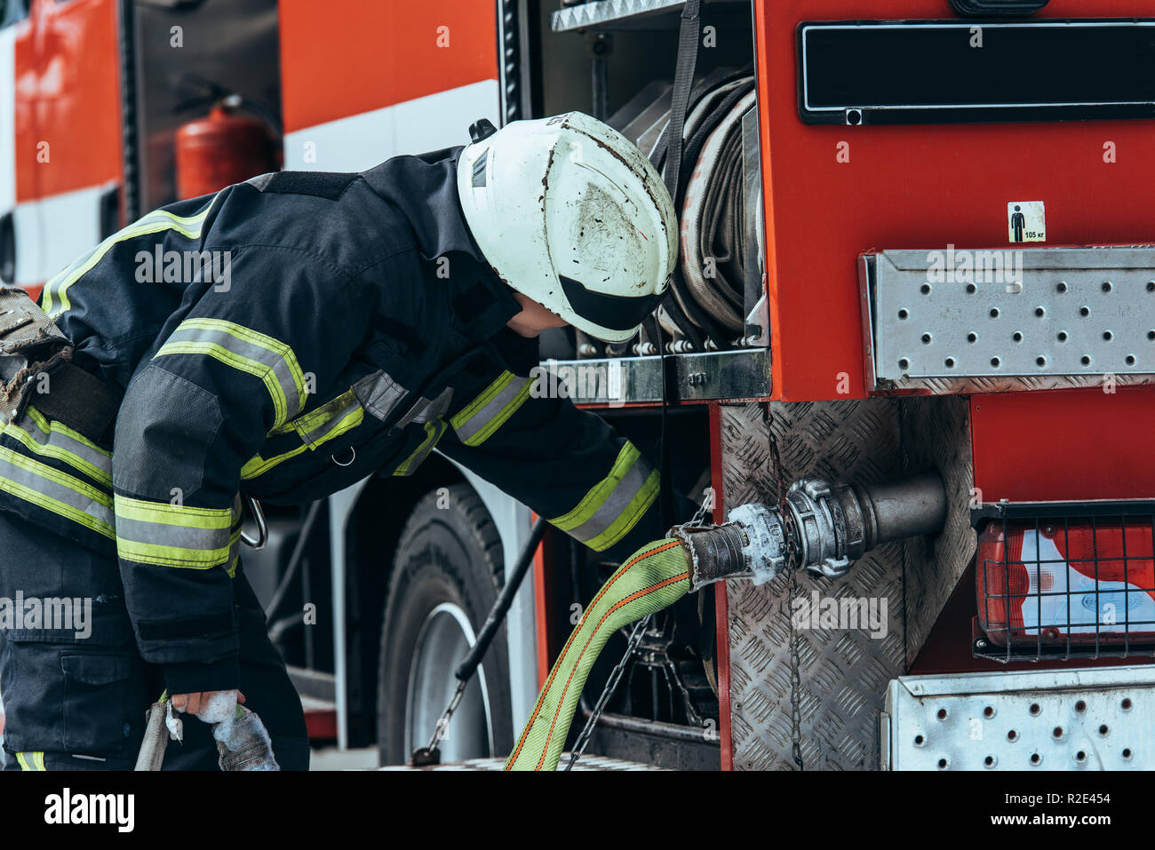 firefighter in protective uniform checking water hose in truck on street Stock Photo