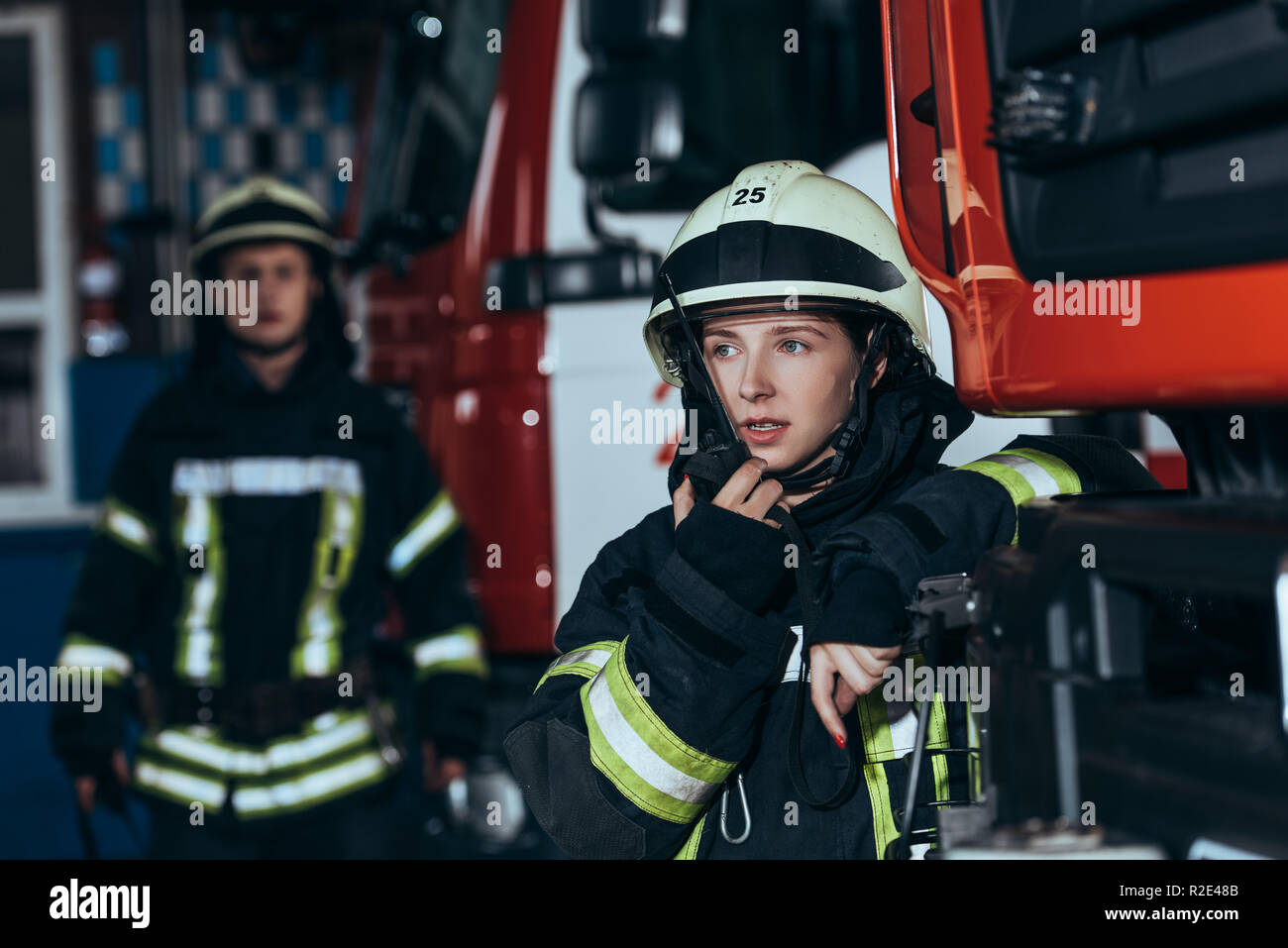 selective focus of female firefighter talking on portable radio set with colleague behind at