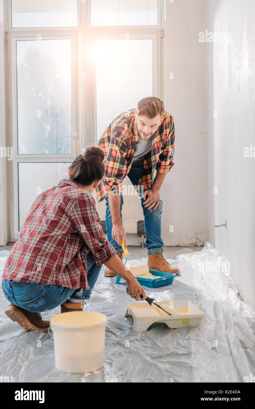 young couple in checkered shirts holding paint rollers and painting wall Stock Photo