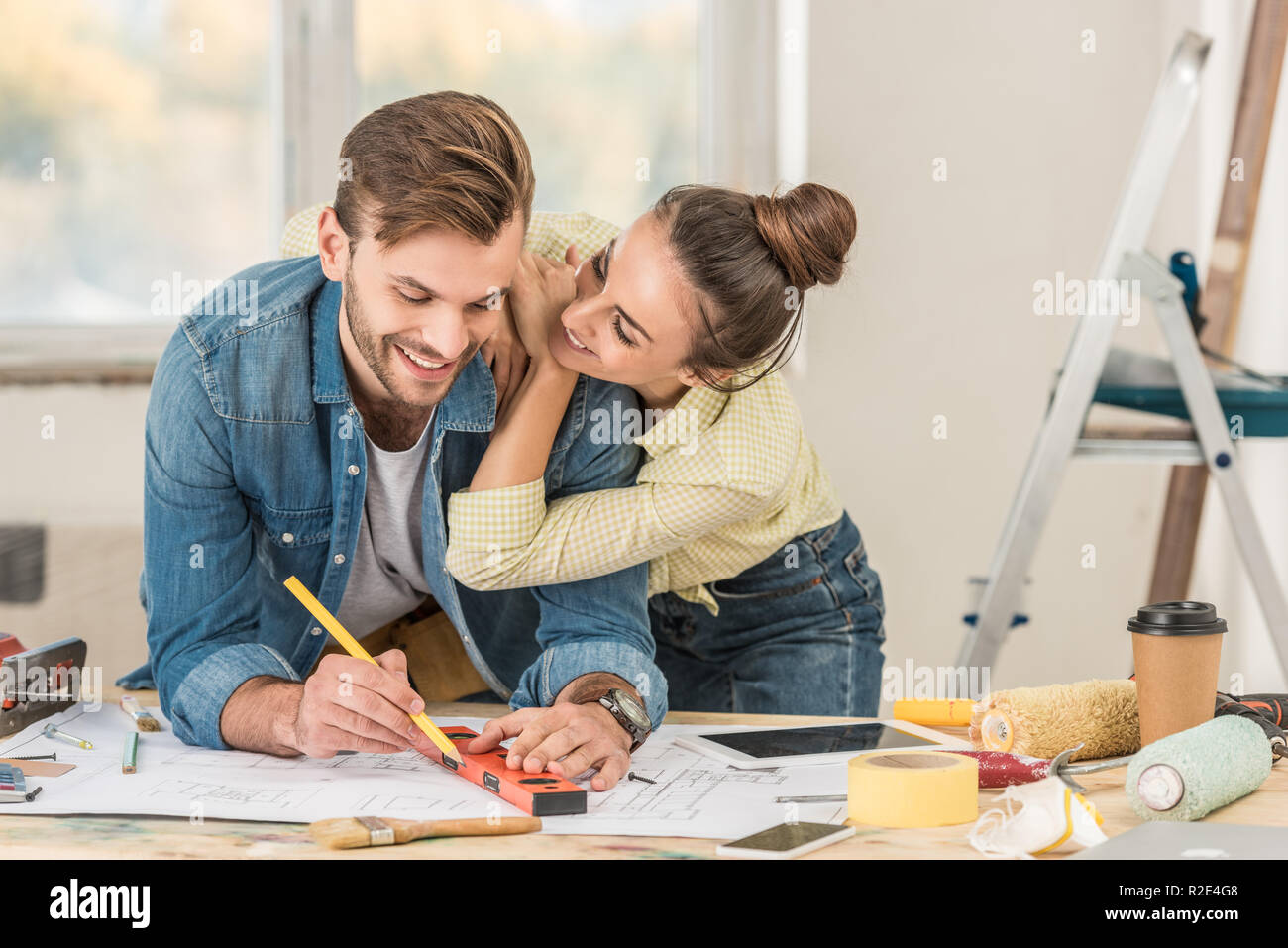 happy young woman hugging smiling boyfriend marking blueprint with